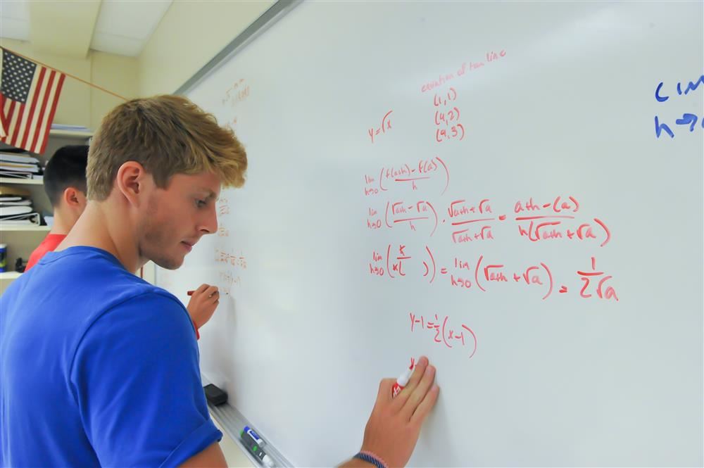 Student solving math problems on a white board in a classroom. Student solving math problems on a white board in a classroom.